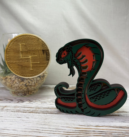 A laser cut wooden cobra decor piece with green and orange details, cut from colored wood from Etched in Favour.
