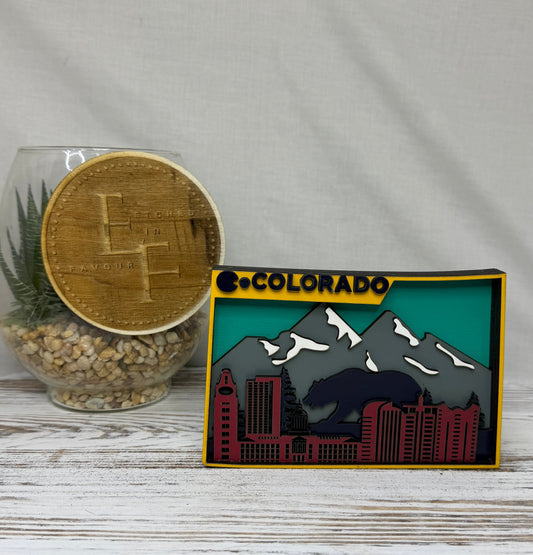 A laser cut multilayered and multicolor wooden Colorado-themed decor piece featuring a stylized mountain and cityscape design with the word 'COLORADO' at the top, with a bear from Etched in Favour.
