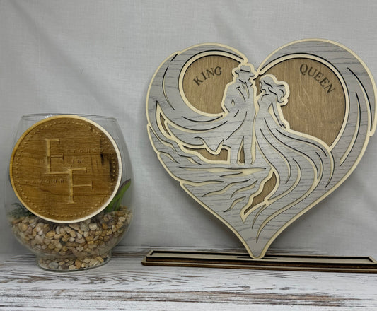 A laser cut heart-shaped wooden decorative piece with laser-cut figures and the words 'KING' and 'QUEEN', from Etched in Favour.