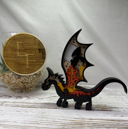 A laser cut multilayer dragon decor piece in black with yellow and orange flame patterns on its wings, from Etched in Favour.