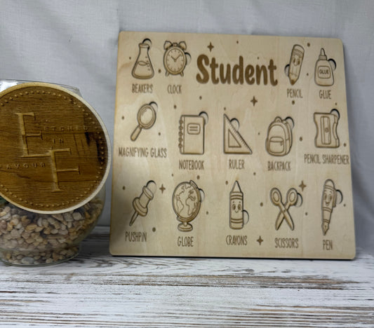 A rectangular wooden children's puzzler laser cut and engraved with school-themed icons and labels such as beaker, clock, pencil, glue, notebook, backpack, scissors, and pen, from Etched in Favour.