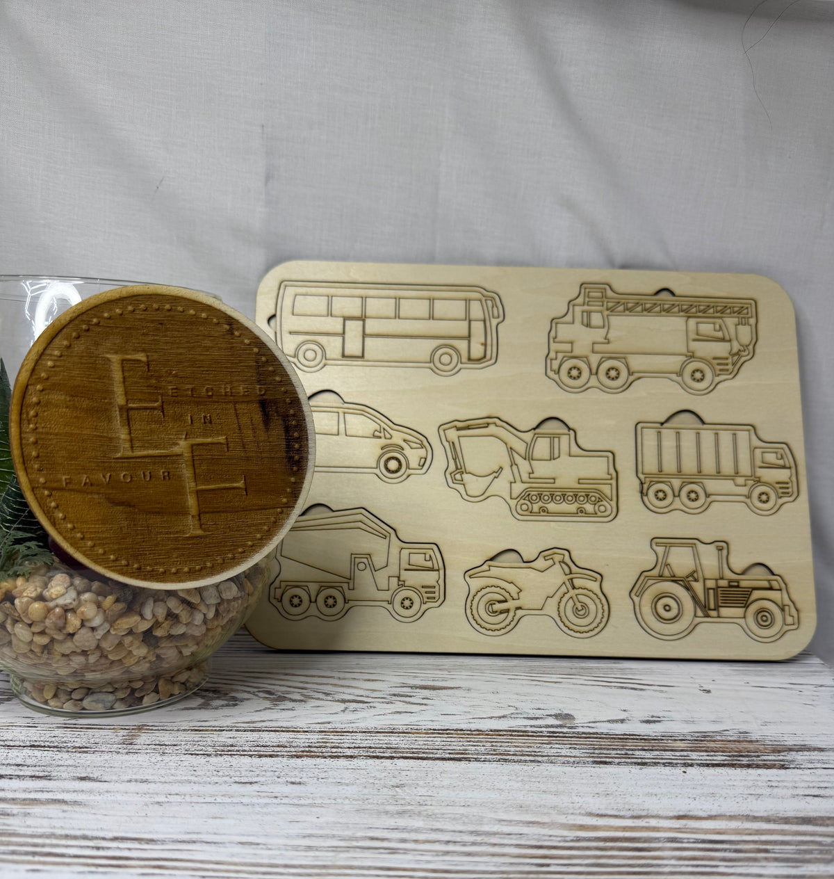 A rectangular wooden puzzle featuring engraved outlines of various vehicles, including a bus, a truck, a bulldozer, a tractor, and a motorcycle for children from Etched in Favour.